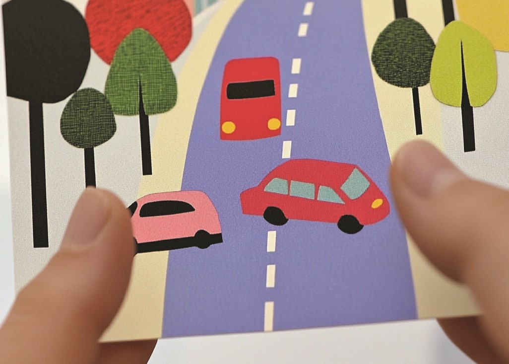 hands holding a card with an illustration of cars on a road